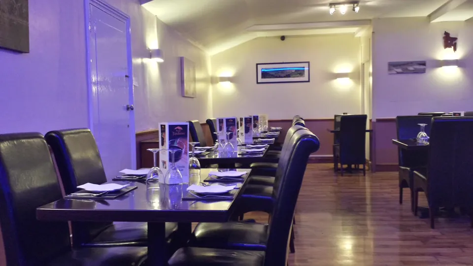 The dining room laid for service: dark tables with folded napkins and upturned glasses, black leather chairs, and a menu card on each table.