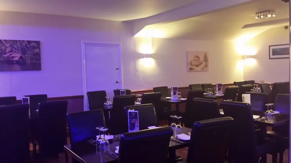 A wide view of the dining room: rows of dark tables and black leather chairs on a wooden floor, with framed pictures on the wall.