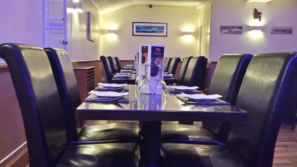 A close view of a table laid for dinner: a plate with a folded napkin, cutlery, two upturned glasses and a menu card, with more tables behind.